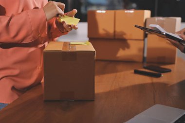 Girişim KOBİ küçük işletme girişimcisi önlük giyen Asyalı kadın dizüstü bilgisayar ve kutu kullanarak çevrimiçi müşterilere, çevrimiçi sme iş fikirlerine satış hazırlamak için siparişleri alır ve gözden geçirir.