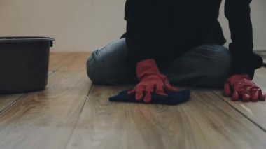 Kırmızı eldivenli bir kadın fırçayla yerleri temizliyor.