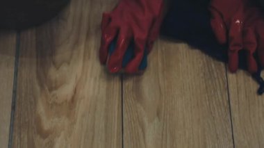 Kırmızı eldivenli adam ahşap zemini temizliyor.