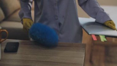 Yakın plan, ofis masasını temizlerken dizüstü bilgisayar kullanan profesyonel temizlikçinin fotoğrafı.