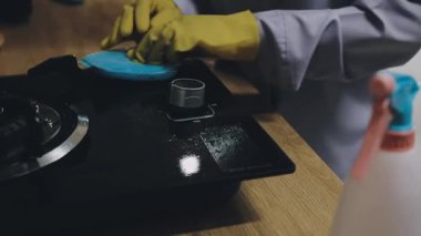 Siyah eldivenli bir adamın eli, siyah bir mutfak sobasını siyah bir gaz sobasıyla temizliyor.