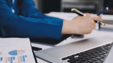 İşadamı laptopta çalışıyor ve masanın üstünde grafikler var.