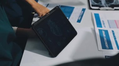 Doktor elinde dijital tablet tutuyor ve hastane ofisinde röntgen filmi gösteriyor.