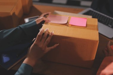 Girişim KOBİ küçük işletme girişimcisi önlük giyen Asyalı kadın dizüstü bilgisayar ve kutu kullanarak çevrimiçi müşterilere, çevrimiçi sme iş fikirlerine satış hazırlamak için siparişleri alır ve gözden geçirir.