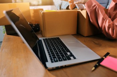 Girişim KOBİ küçük işletme girişimcisi önlük giyen Asyalı kadın dizüstü bilgisayar ve kutu kullanarak çevrimiçi müşterilere, çevrimiçi sme iş fikirlerine satış hazırlamak için siparişleri alır ve gözden geçirir.