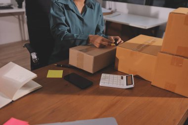 Girişim KOBİ küçük işletme girişimcisi önlük giyen Asyalı kadın dizüstü bilgisayar ve kutu kullanarak çevrimiçi müşterilere, çevrimiçi sme iş fikirlerine satış hazırlamak için siparişleri alır ve gözden geçirir.