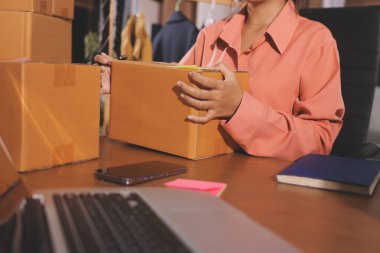 Girişim KOBİ küçük işletme girişimcisi önlük giyen Asyalı kadın dizüstü bilgisayar ve kutu kullanarak çevrimiçi müşterilere, çevrimiçi sme iş fikirlerine satış hazırlamak için siparişleri alır ve gözden geçirir.