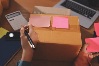 Girişim KOBİ küçük işletme girişimcisi önlük giyen Asyalı kadın dizüstü bilgisayar ve kutu kullanarak çevrimiçi müşterilere, çevrimiçi sme iş fikirlerine satış hazırlamak için siparişleri alır ve gözden geçirir.