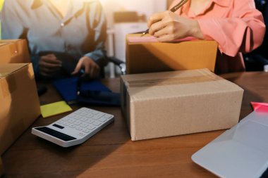 Girişim KOBİ küçük işletme girişimcisi önlük giyen Asyalı kadın dizüstü bilgisayar ve kutu kullanarak çevrimiçi müşterilere, çevrimiçi sme iş fikirlerine satış hazırlamak için siparişleri alır ve gözden geçirir.