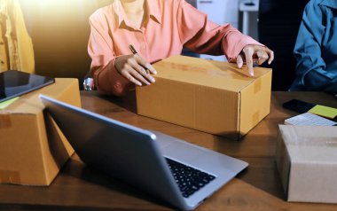 Girişim KOBİ küçük işletme girişimcisi önlük giyen Asyalı kadın dizüstü bilgisayar ve kutu kullanarak çevrimiçi müşterilere, çevrimiçi sme iş fikirlerine satış hazırlamak için siparişleri alır ve gözden geçirir.