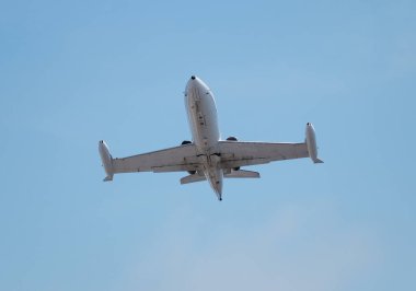 A low-angle view of a jet aircraft flying overhead against a clear blue sky. The underside of the plane is visible, showcasing its streamlined design and powerful engines. This perspective highlights the aircraft's movement and engineering precision clipart