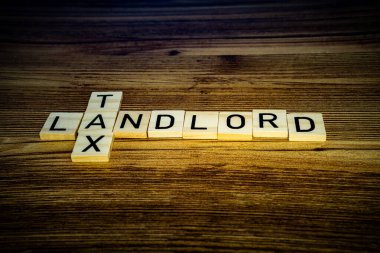 Ahşap arkaplan bulmacası üzerine ahşap harflerle ev sahibi vergi kavramı