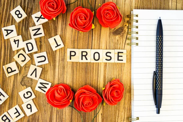 Prose flat lay made of laser-engraved letters on blank line notebook and pen with scattered letters and roses