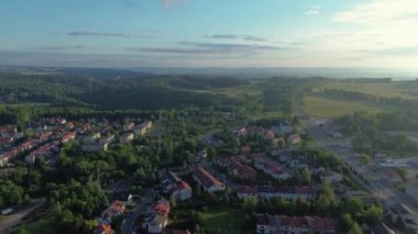 Walbrzych, Polonya 'dan uçarak uzaklaşıyor, şehirlerdeki yerleşim bölgelerinde, yemyeşil ağaçların arasında yuvarlanan tepelere doğru kümelenmiş evler ve arka planda Ksiaz Kalesi olan geniş yeşil bir orman var.