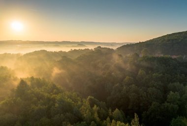 Güneşin doğuşuyla birlikte ormanlık bir vadiyi saran sabah sisi sakin bir manzaranın yakınındadır.