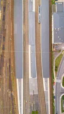 Birçok raylı bir tren istasyonunun hava görüntüsü ve gündüz vakti banliyödeki bir platformda tren.