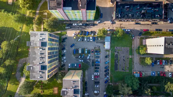 Kalabalık bir otoparkın havadan görüntüsü gündüz vakti bir şehirde konut binaları ve yeşilliklerle çevrili.