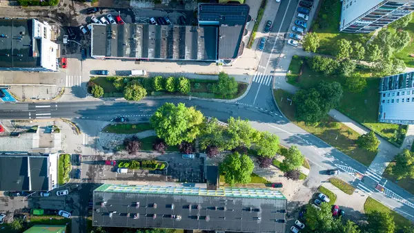 Gündüz vakti şehir sokaklarının, yeşil alanların ve park halindeki arabaların hava görüntüsü.