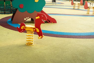Sabahın erken saatlerinde halka açık bir parkta renkli oyun alanlarıyla çevrili bir bahar binicisi oyuncağı.