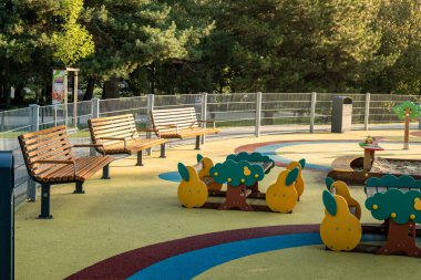 Sabahın erken saatlerinde sakin bir halk parkında renkli oyun alanı yapıları ve boş banklar var.