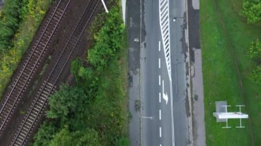 Etrafı yeşilliklerle çevrili sessiz bir demiryolu ve yol kesişiminin havadan görüntüsü
