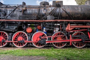 Paslı bir buharlı trenin tekerlekleri ve makineleri gün ışığında sakin bir yerde.