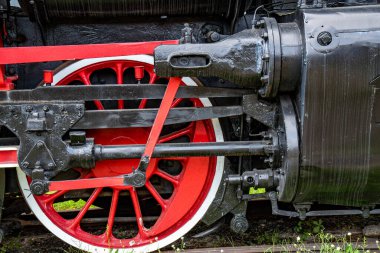 Kırmızı tekerlekleri ve mekanik parçaları olan eski paslı bir buhar treni motorunun detaylı görüntüsü