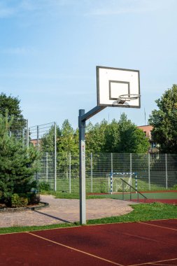 Açık hava basketbol sahasının arka planında açık mavi gökyüzünün altında canlı yeşil bir çember var.