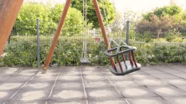 Güneşli bir parkta boş bir salıncak ve arka planda öğleden sonraları yeşil ağaçlar.