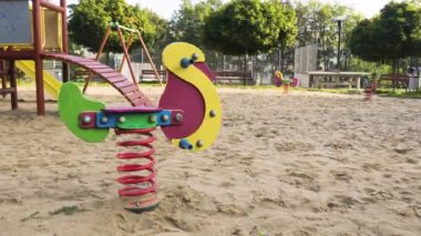 Güneşli bir parkta, arka planda kum ve ağaçlar olan renkli oyun alanı ekipmanları, çocukların eğlence ve oyun zamanı için idealdir.