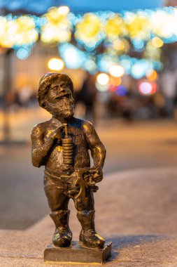 Wrocaw, Polonya - 01.18.2024: Market Meydanı, Wroclaw 'da elinde bir müzik aleti bulunan büyüleyici bir bronz cüce gururla duruyor. Akşam ışıkları sıcak bir atmosfer yaratıyor, ziyaretçileri cezbediyor canlı meydanı keşfediyorlar..