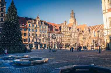 Wrocaw, Polonya - 01.18.2024: Ziyaretçiler, Polonya 'nın Wroclaw kentindeki Pazar Meydanı' nda tarihi binalar ve bayram süslemeleriyle çevrili canlı bir kış gününün keyfini çıkararak şenlikli bir atmosfer yarattılar..