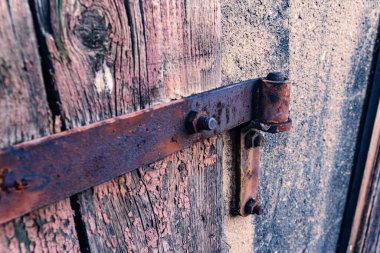 Kırsal alanda paslı menteşeleri olan eskimiş ahşap bir kapı.