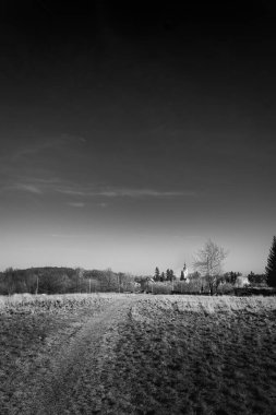 Gökyüzünün altındaki uzak bir kiliseye bakan boş bir tarlanın siyah ve beyaz manzarası