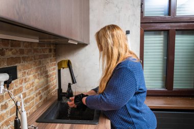 Modern mutfakta elleri yıkayan kadın tuğla duvarlı ve gün ışığında geniş pencereli.