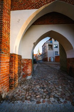 Resimli bir kemer yolu kaldırım taşlı bir yola açılıyor, ılık gün batımı ışığında yıkanmış, gezginleri tuhaf bir kasabaya davet ediyor..