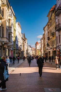 Torun 'un hareketli caddeleri, güneş ışığını ve berrak mavi gökyüzünün altındaki canlı atmosferi emiyor..