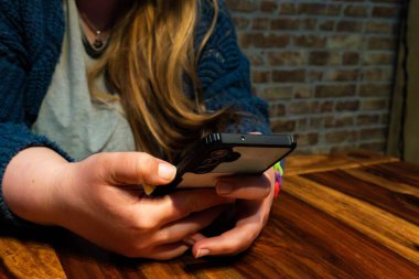 Kafkas anne ahşap bir masada otururken akıllı telefonuyla gelişigüzel iletişim kuruyor, sıcak ışık sakin bir ortam yaratıyor..