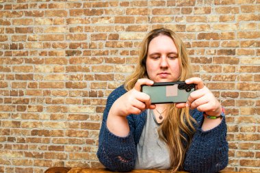 Güzel bir anne, kendi dünyasına dalmış, akıllı telefonuyla meşgul olur. Tuğladan örülü bir duvara yaslanmış, huzur saçar..