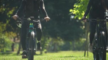 Güneşli bir yaz gününde parkta bisiklet süren genç bir çift..