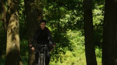 Ağaçların gölgesinde bisiklete binen genç bir kadın ve partneri onu takip ediyor..