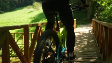 Güneşli bir yaz gününde, park köprüsünün üzerinden bisikletle geçen genç bir çift..