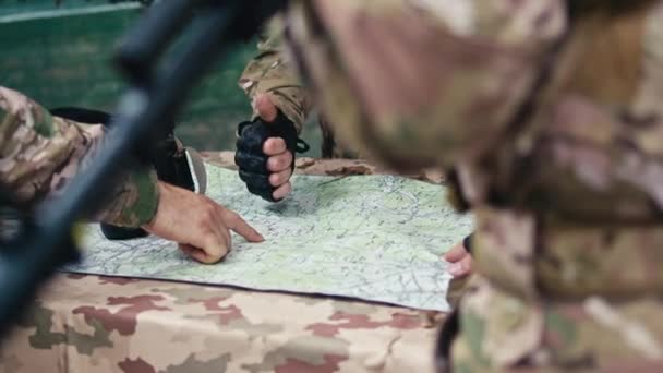 Close-up of military personnel planning action. Commanders in uniform, pointing at a map, discussing strategy. Shot from behind a soldier.