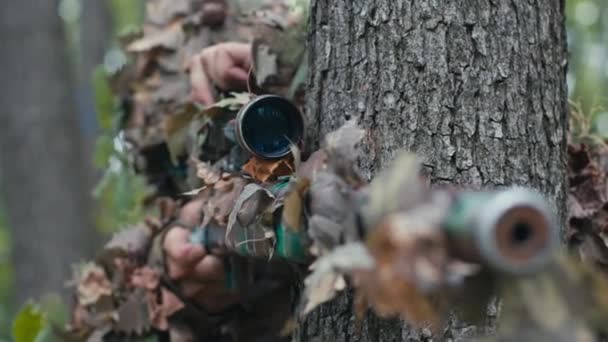 一棵树后的伪装狙击手通过高精度瞄准镜瞄准一个遥远的目标 — 图库视频影像