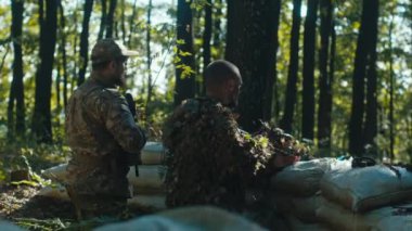 İki yetenekli asker, bir keskin nişancı ve bir piyade, kum torbası sığınağının arkasında stratejik olarak konumlanmışlar..