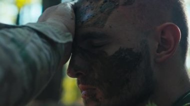 Bir asker, kamuflaj için kamufle olan kum torbası sığınağında arkadaşının yüzüne çamur sürer..