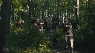 Bir hava aracı onları takip ederken bir askeri birlik ormanlık alanda dikkatli bir şekilde koşuyor..