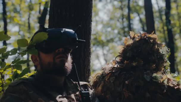 两名士兵 一名伪装狙击手和一名无人驾驶飞机操作员 在树后战略性地站稳了脚跟 — 图库视频影像