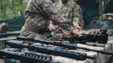 Askeri teçhizatlı askerler güne hazırlanmaya odaklanır. Kurşun geçirmez yelek de dahil olmak üzere savunma ekipmanlarını giyip çıkarıyorlar..