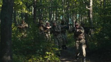 Bir askeri birlik ağaçların arasından hızla geçiyor ve bir dron onları takip ederken etraflarına bakınıyor..
